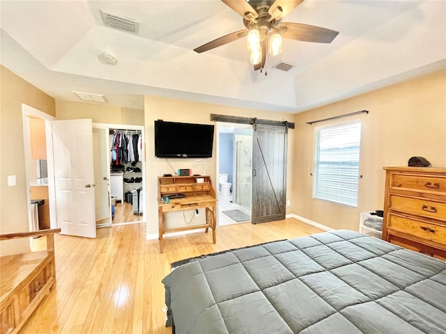 bedroom featuring a tray ceiling, wood-type flooring, a barn door, and ceiling fan