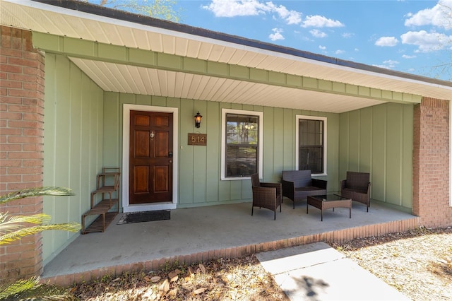 view of exterior entry with a porch, brick siding, and board and batten siding