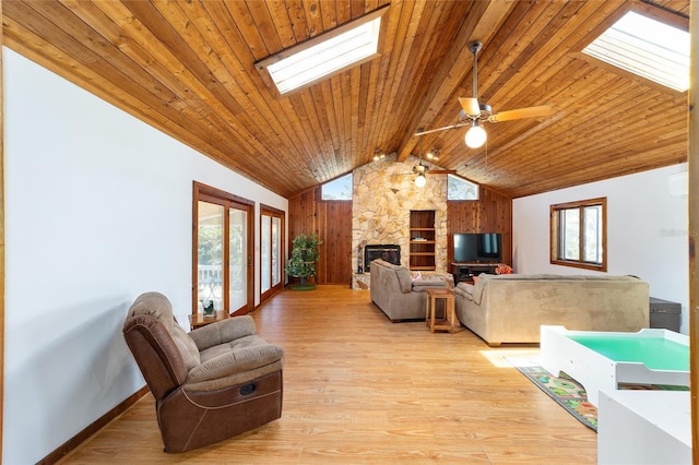 living area featuring a skylight, wooden ceiling, beamed ceiling, a stone fireplace, and light wood-type flooring