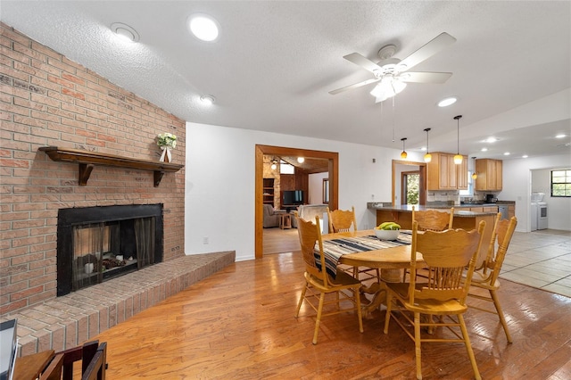 dining space featuring washer and dryer, light wood-type flooring, a fireplace, and a textured ceiling