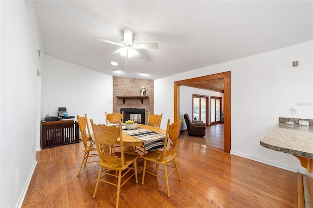 dining space featuring ceiling fan, a fireplace, wood finished floors, and baseboards