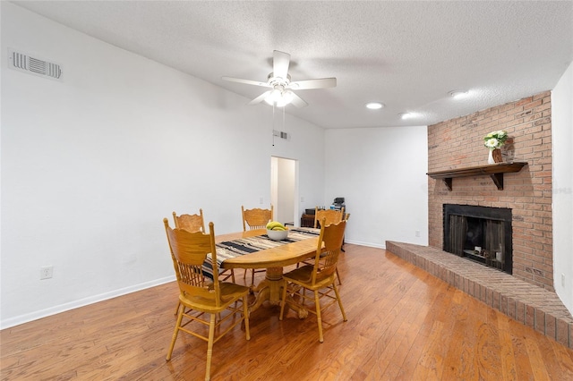 dining room with a brick fireplace, visible vents, baseboards, and light wood finished floors