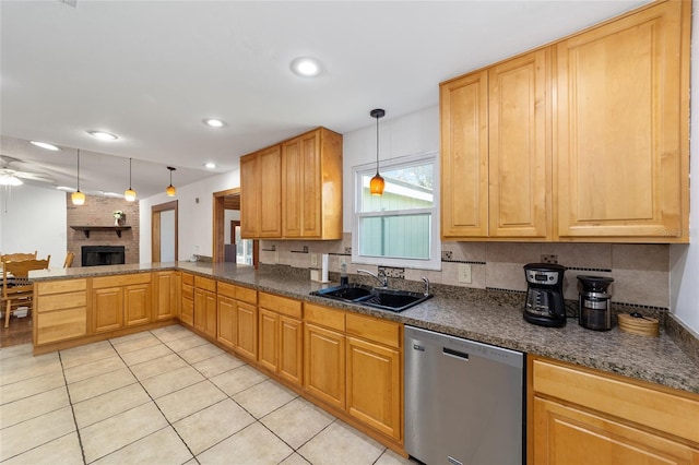 kitchen with a ceiling fan, a peninsula, stainless steel dishwasher, a brick fireplace, and a sink