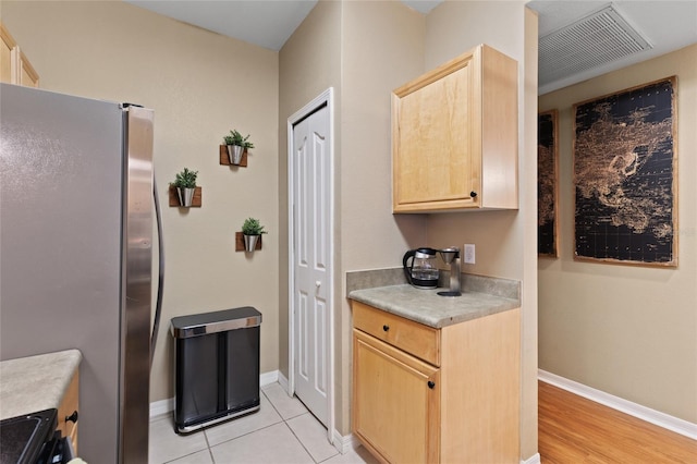 kitchen with light brown cabinets, baseboards, light countertops, and freestanding refrigerator