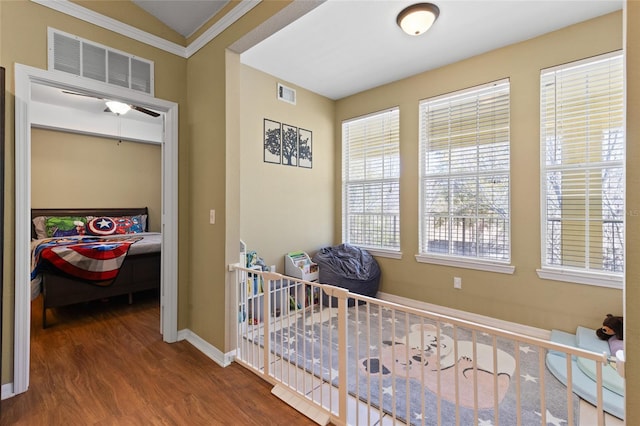 corridor featuring ornamental molding, wood finished floors, visible vents, and baseboards