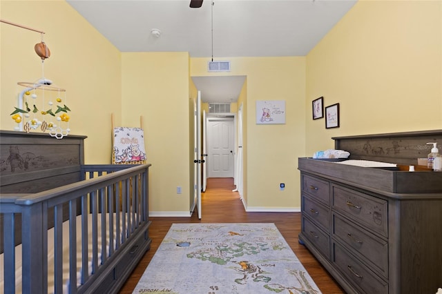 bedroom with a ceiling fan, visible vents, baseboards, a nursery area, and dark wood finished floors