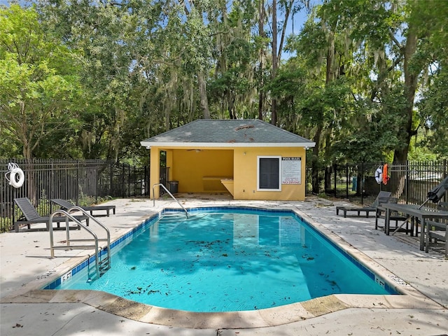 community pool with an outbuilding, a patio area, and fence