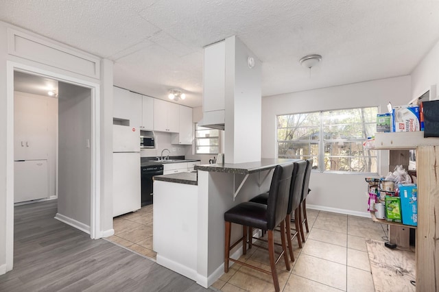 kitchen with white cabinets, dark countertops, stainless steel microwave, a breakfast bar, and freestanding refrigerator