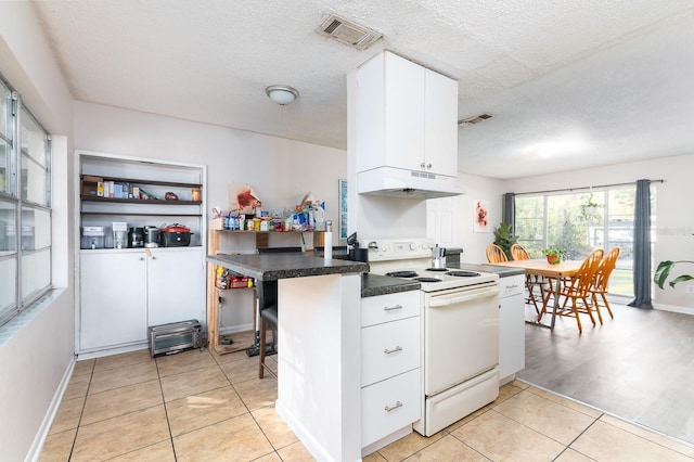 kitchen featuring visible vents, under cabinet range hood, white cabinetry, and electric range