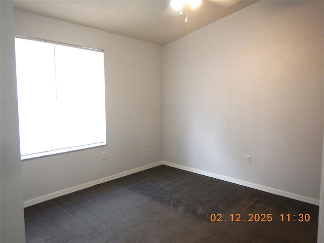 unfurnished room featuring baseboards, dark carpet, and a ceiling fan