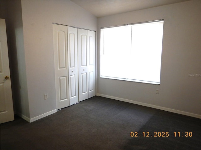 unfurnished bedroom with dark colored carpet, a closet, and baseboards