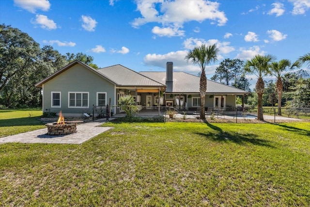 rear view of house with an outdoor fire pit, a lawn, a patio, a chimney, and metal roof