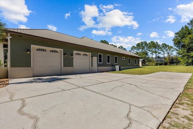 view of front of house featuring metal roof, an attached garage, cooling unit, driveway, and a front yard