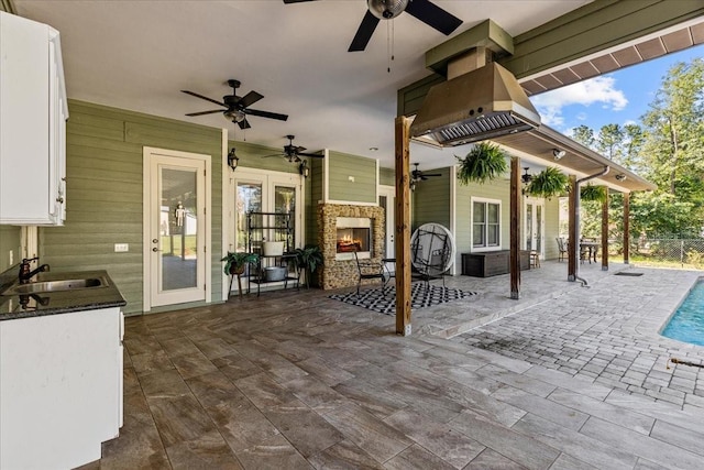 view of patio / terrace featuring a lit fireplace, a ceiling fan, and a sink