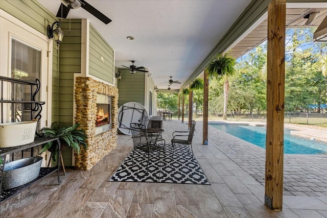 view of patio with a fenced in pool, an outdoor stone fireplace, and a ceiling fan