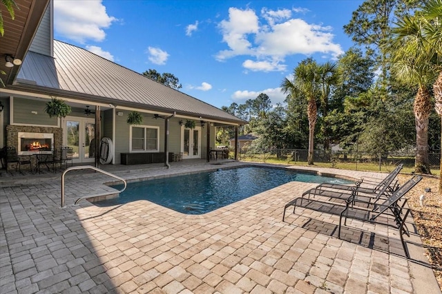 view of swimming pool with an outdoor stone fireplace, french doors, a patio, ceiling fan, and fence