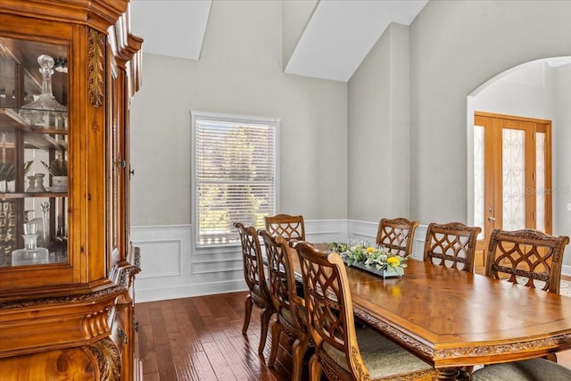 dining area with arched walkways, dark wood finished floors, and wainscoting