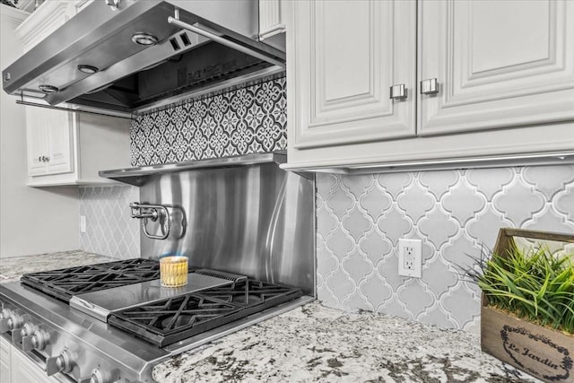 kitchen with wall chimney exhaust hood, light stone counters, white cabinetry, backsplash, and gas cooktop