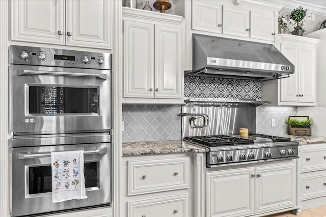 kitchen featuring light stone counters, white cabinets, appliances with stainless steel finishes, ventilation hood, and tasteful backsplash