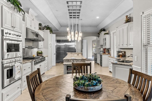 kitchen with arched walkways, under cabinet range hood, stainless steel appliances, a center island, and light stone countertops