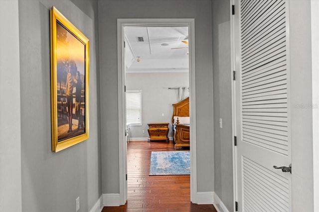 hallway featuring dark wood-style floors, visible vents, baseboards, and ornamental molding