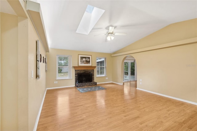 unfurnished living room featuring ceiling fan, a fireplace, light hardwood / wood-style floors, and lofted ceiling with skylight