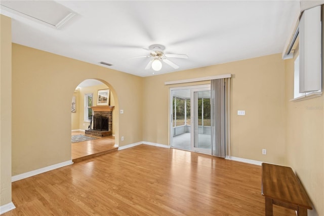 empty room featuring ceiling fan, a brick fireplace, and light wood-type flooring