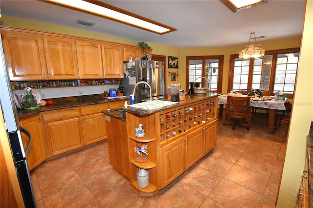 kitchen featuring a healthy amount of sunlight, stainless steel fridge, decorative light fixtures, and an island with sink