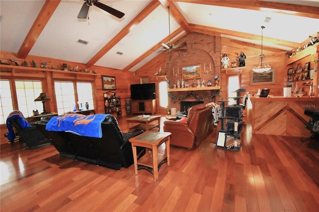 living room with ceiling fan, wood-type flooring, a brick fireplace, beamed ceiling, and wood walls