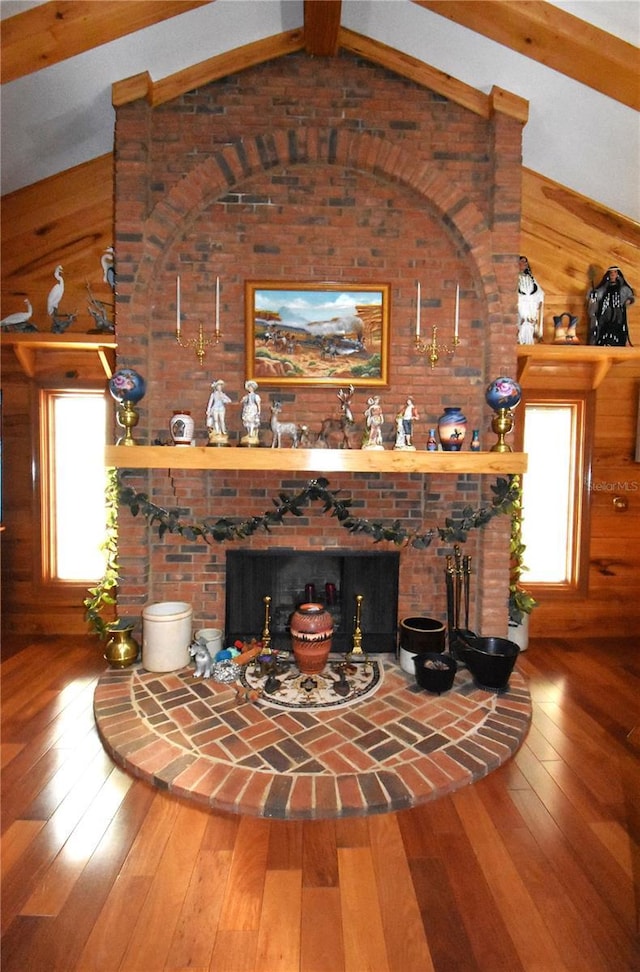 unfurnished living room with lofted ceiling with beams, a wealth of natural light, a brick fireplace, and hardwood / wood-style floors