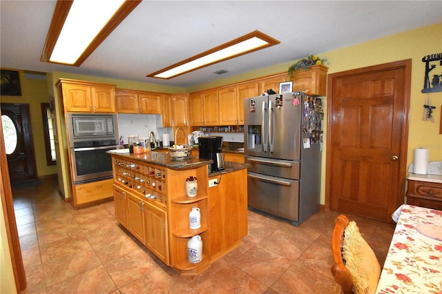 kitchen with a kitchen island with sink, stainless steel appliances, and dark stone counters