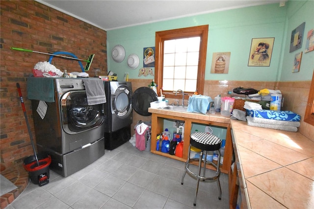 laundry room with light tile patterned flooring, brick wall, sink, and washer and clothes dryer