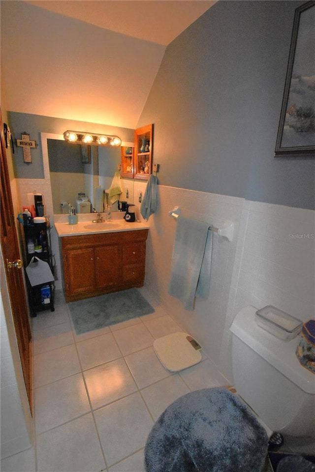 bathroom featuring lofted ceiling, tile patterned flooring, tile walls, vanity, and toilet