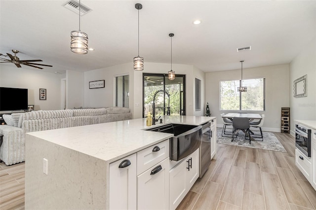 kitchen with pendant lighting, white cabinetry, sink, stainless steel appliances, and a center island with sink