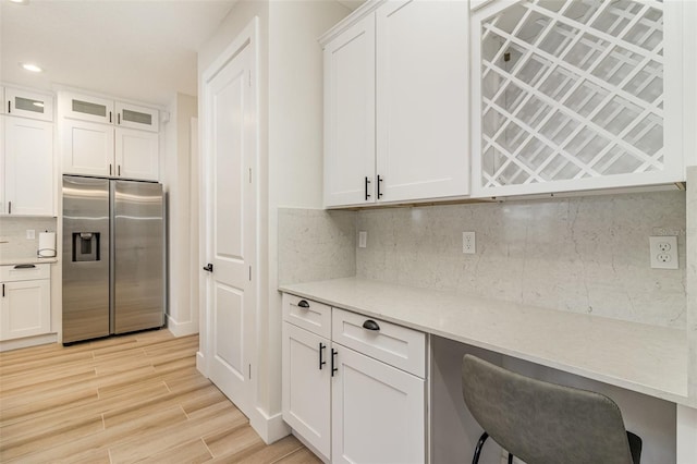 kitchen featuring white cabinetry, backsplash, stainless steel refrigerator with ice dispenser, built in desk, and light hardwood / wood-style floors