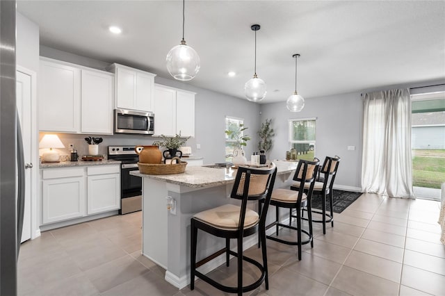 kitchen with appliances with stainless steel finishes, white cabinets, decorative light fixtures, and an island with sink