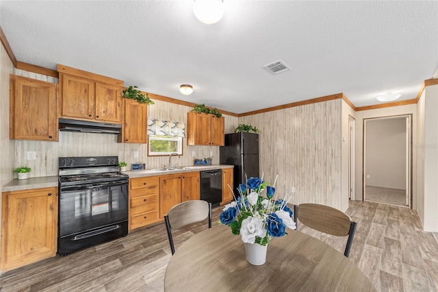 kitchen with light wood-style flooring, under cabinet range hood, light countertops, ornamental molding, and black appliances