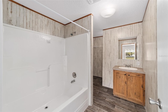 bathroom with wood finished floors, tub / shower combination, a textured ceiling, vanity, and wood walls