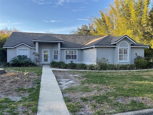 single story home featuring a shingled roof, a front yard, and stucco siding