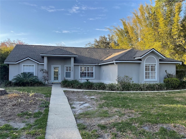 ranch-style home with a shingled roof, a front lawn, and stucco siding