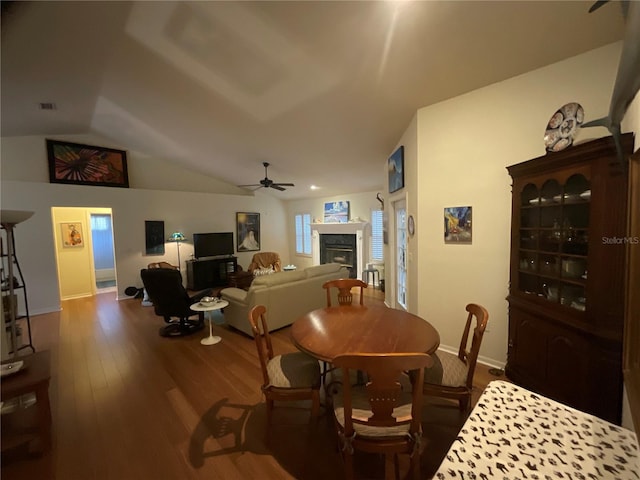 dining space featuring visible vents, a glass covered fireplace, ceiling fan, vaulted ceiling, and wood finished floors