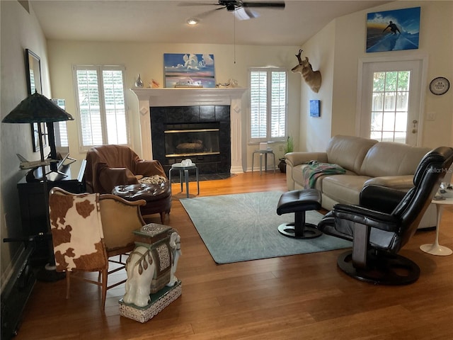 living area featuring a ceiling fan, a tile fireplace, and wood finished floors