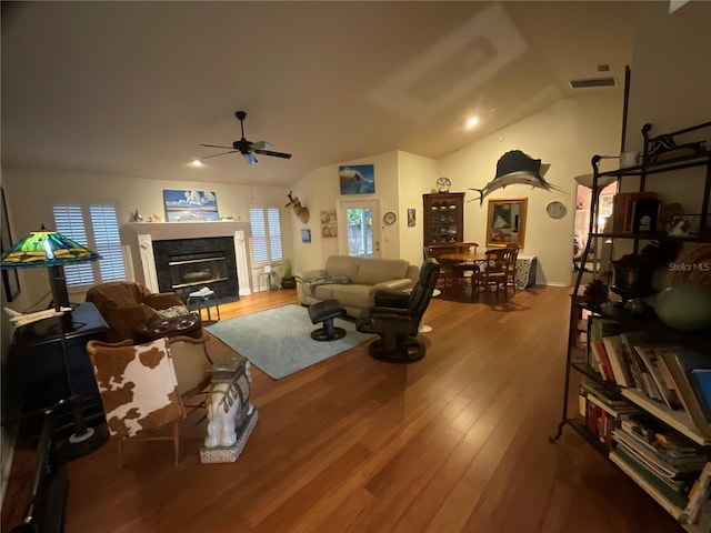 living room featuring lofted ceiling, visible vents, a ceiling fan, a glass covered fireplace, and wood finished floors