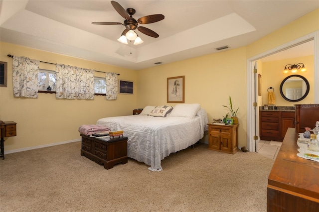 bedroom featuring visible vents, light carpet, a tray ceiling, ensuite bath, and ceiling fan