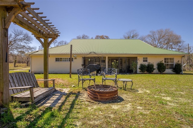 rear view of property featuring a pergola, an outdoor fire pit, a yard, and metal roof