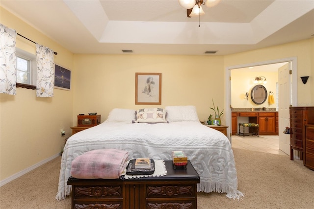 bedroom with a raised ceiling, visible vents, and connected bathroom