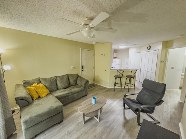 living area with a textured ceiling, light wood-type flooring, and baseboards