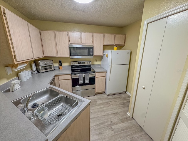 kitchen featuring wood finish floors, stainless steel appliances, light brown cabinets, a sink, and a textured ceiling