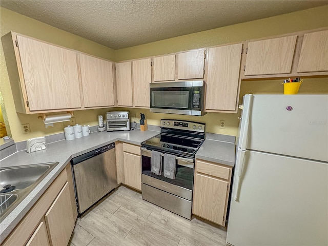 kitchen with light brown cabinetry, appliances with stainless steel finishes, light wood-type flooring, and a sink