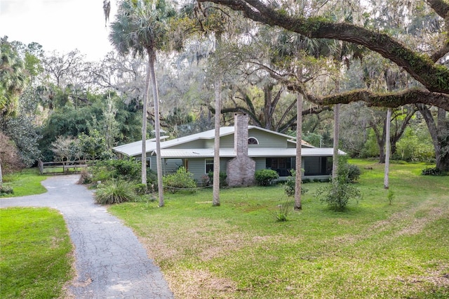 view of front of property featuring aphalt driveway, a chimney, and a front lawn